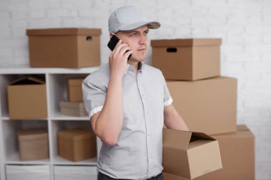 Posta teslimatı ve iş adamları konsepti. Depodaki adam elinde kutuyla telefonla arıyor.