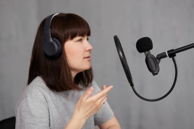 Genç çekici bir kadının portresi mikrofon ve kulaklıkla podcast yapıyor.