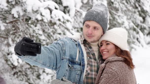 快乐的年轻夫妇在冬天的森林里用智能手机拍下了自己的照片 — 图库视频影像