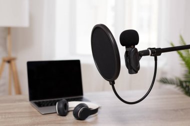 Podcast, ses kaydı ve blog konsepti - mikrofona pop filtresi ile yakın çekim ve parlak ev ofisteki ekranda kopya alanı olan dizüstü bilgisayar