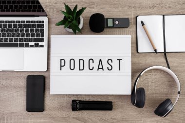 Podcast konsepti - düz zemin üzerinde dizüstü bilgisayarı, mikrofonu, kulaklığı, akıllı telefonu ve not defteri olan ışık kutusunu kapatın