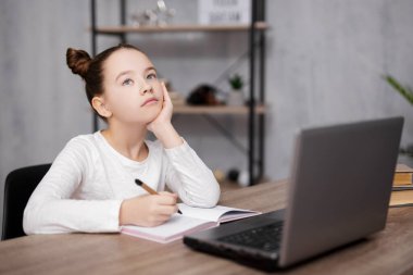 Okul, ödev ve uzaktan eğitim konsepti - ev ödevi yapan ve evde online çalışmak için dizüstü bilgisayar kullanan sıkılmış veya düşünceli bir kızın portresi