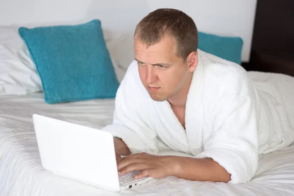 Homem com roupão usando laptop no quarto de hotel — Fotografia de Stock