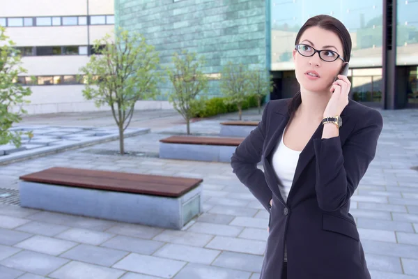 Beautiful business woman talking by phone on street against offi — Stock Photo, Image