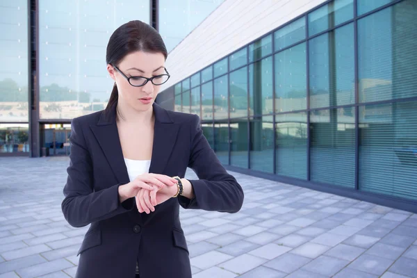 Business woman checks time on her wrist watch standing on street — Stock Photo, Image