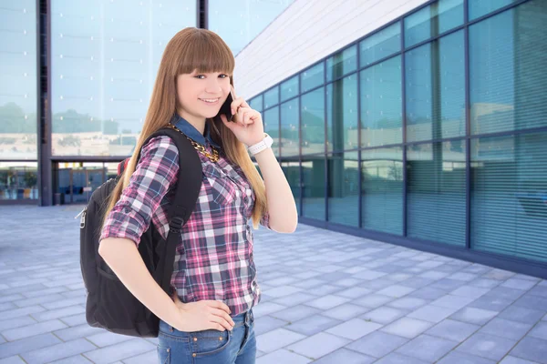 Teenage girl talking by phone standing on street against school — Stock Photo, Image