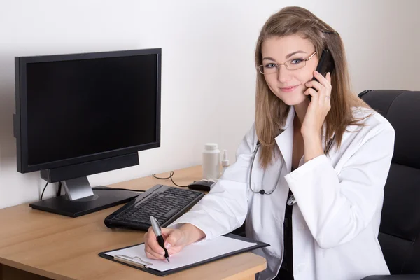 Young woman doctor talking by phone in her office — Stock Photo, Image