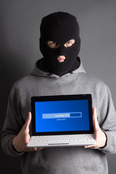 Gemaskerde man met laden computer over grijs — Stockfoto