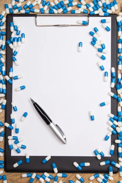 Heal of pills, clipboard and pen on wooden table — Stock Photo, Image