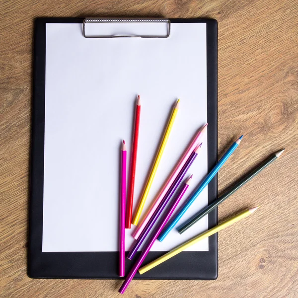 Colored drawing pencils and clipboard with blank paper on wooden — Stock Photo, Image