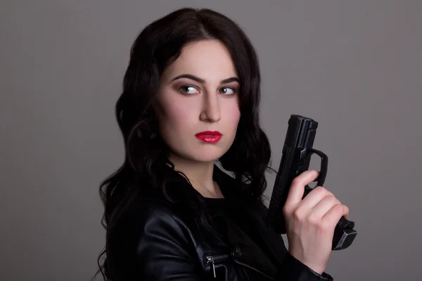 Retrato de uma jovem mulher bonita com arma sobre cinza — Fotografia de Stock