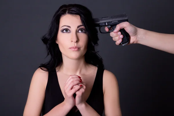 Jovem bela mulher refém e mão masculino com arma sobre cinza — Fotografia de Stock