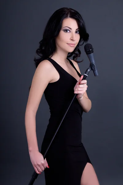 Young beautiful woman singer with microphone over grey — Stock Photo, Image