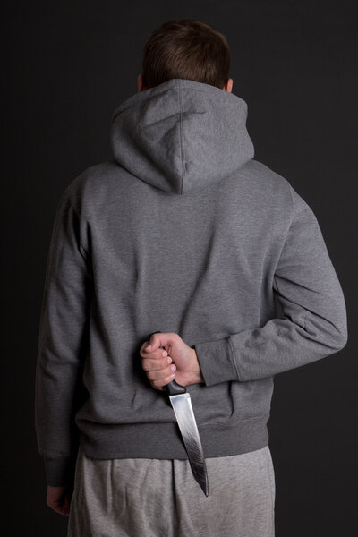 man hiding knife behind his back over grey