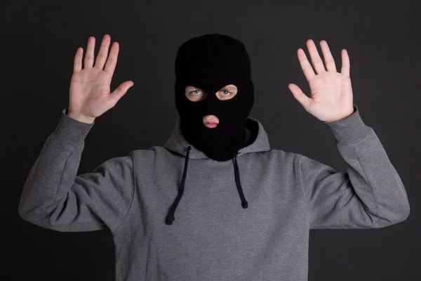Mannen i svart mask håller händerna upp över grå — Stockfoto