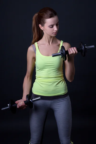 Portrait of beautiful sporty woman with dumbbells over grey — Stock Photo, Image