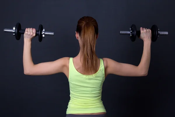 Back view of sporty woman with dumbbells over grey — Stock Photo, Image