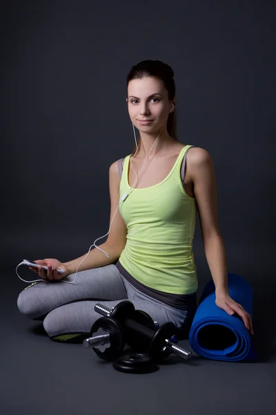 Young sporty woman sitting and listening music with phone over g — Stock Photo, Image
