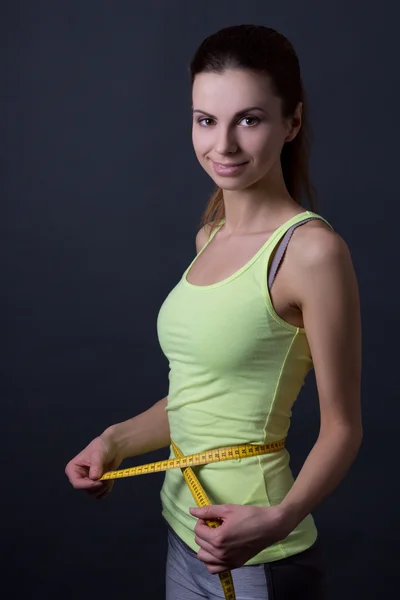 Beautiful slim sporty woman with measure tape over grey — Stock Photo, Image