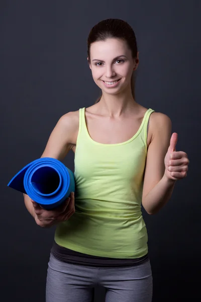 Jonge vrouw in sport slijtage poseren met yoga mat en duimen omhoog ov — Stockfoto