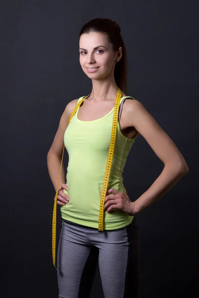 Young beautiful slim sporty woman with measure tape over grey — Stock Photo, Image