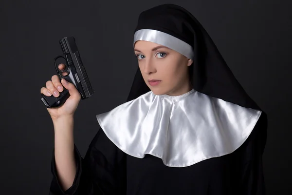 Portrait of young woman nun with gun over grey — Stock Photo, Image