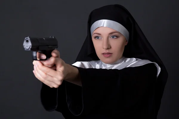 Young woman nun shooting with gun over grey — Stock Photo, Image