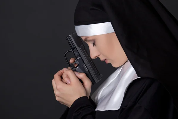 Young woman nun praying with gun over grey — Stock Photo, Image