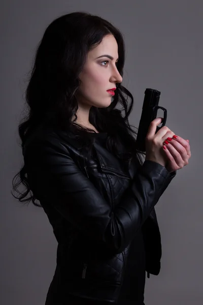 Portret van sexy vrouw in zwart met pistool over grijs Stockfoto