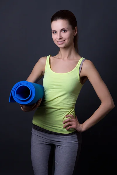 Young woman in sports wear with yoga mat over grey — Stock Photo, Image