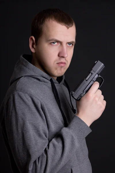 Young man criminal holding gun over grey — Stock Photo, Image