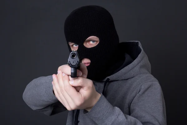 Criminoso mascarado mirando com a arma sobre cinza — Fotografia de Stock