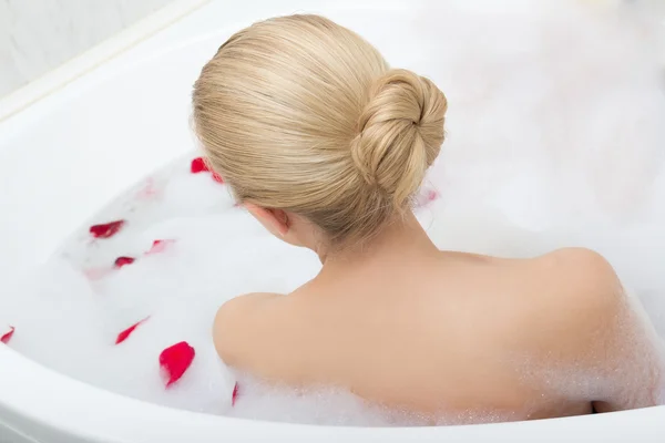 Vista de mulher relaxante em banheira com pétalas de flor vermelha traseira — Fotografia de Stock