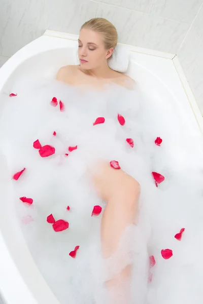 Belle femme se détendre dans le bain aux pétales de fleurs rouges — Photo