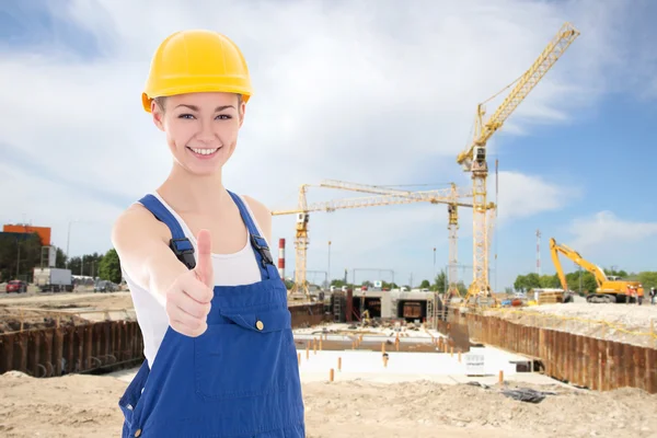 Lycklig kvinna builder i blå overaller tummen upp — Stockfoto