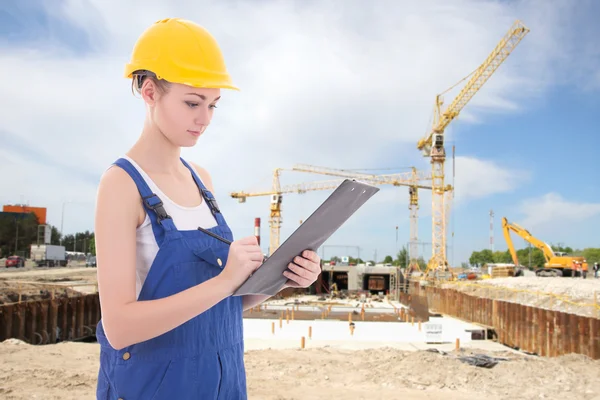 Young attractive woman builder writing something in clipboard — Stock Photo, Image