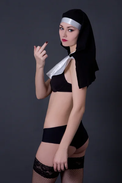 Sexy woman nun in lingerie showing middle finger over grey — Stock Photo, Image