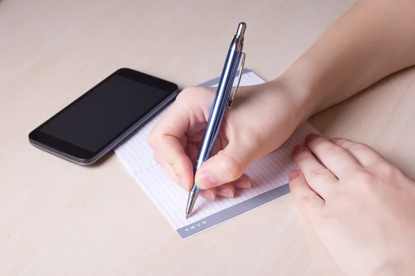Perto da mão feminina com caneta, caderno e telefone — Fotografia de Stock