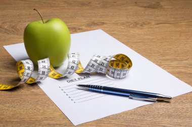 Kağıt diyet planı, kalem, masada elma ve ölçü birimi teyp ile