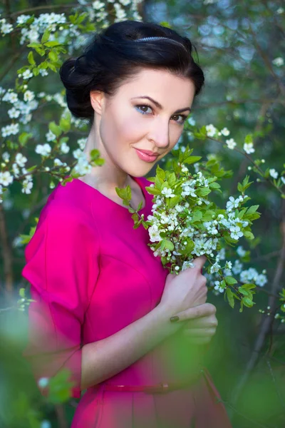 Vacker brunett kvinna i rosa klänning i blommande cherry tree g — Stockfoto