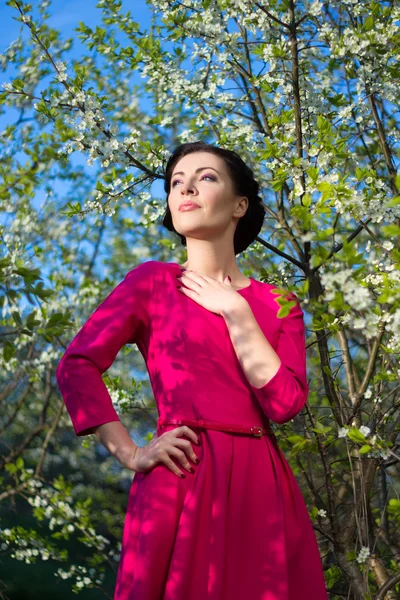 Belle jeune femme en robe rose posant dans jardin fleuri — Photo