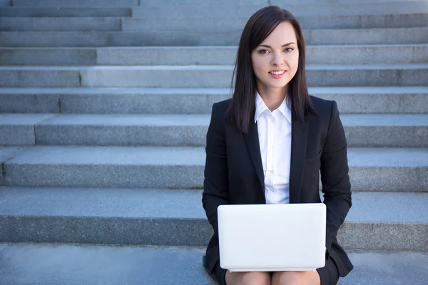 Beautiful business woman sitting on stairs with laptop — Stock Photo, Image
