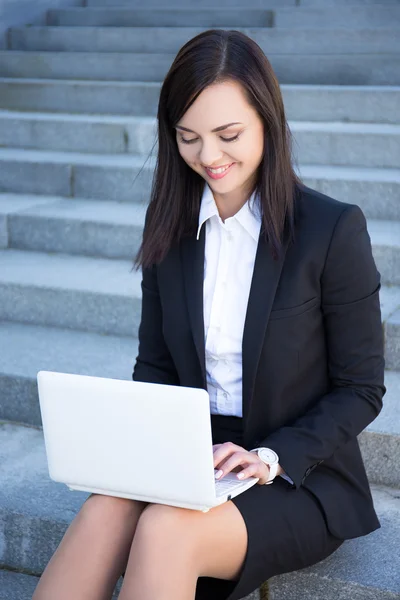 Happy beautiful business woman sitting on stairs and using lapto — Stock Fotó