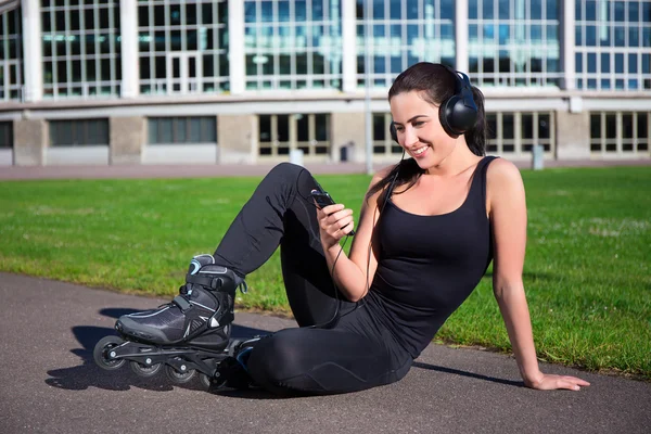 Щаслива жінка в роликових ковзанах сидить і слухає музику в парку — стокове фото