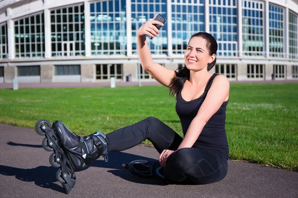 Šťastná žena v kolečkové brusle sedí a že selfie foto na — Stock fotografie