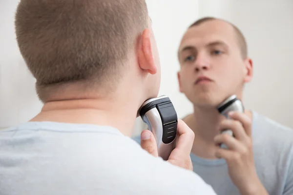 Jonge man in de spiegel scheren met elektrisch scheerapparaat — Stockfoto