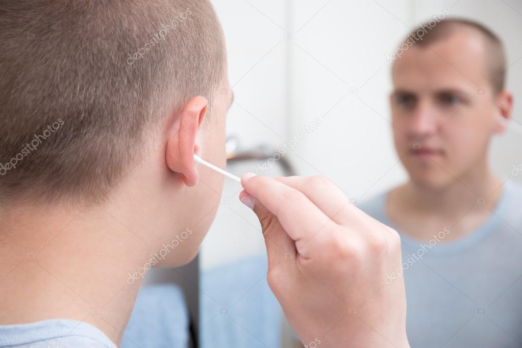 man cleans his ear with a cotton swab 