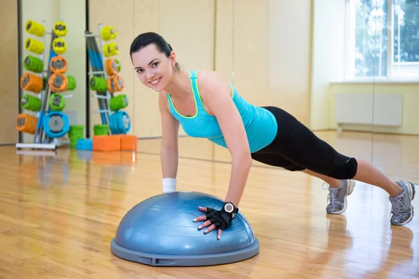 Hermosa mujer delgada haciendo push ups con la bola de bosu en gimnasio —  Fotos de Stock