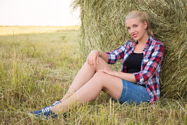 Beautiful blonde woman sitting in field with haystacks — Stock Photo, Image