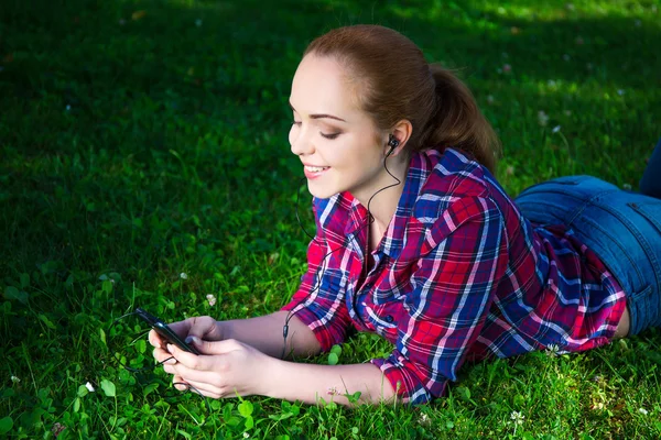 Tonårsflicka som ligger och lyssnar musik med smart telefon i park — Stockfoto